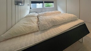 A single bed with a quilted mattress and a black headboard in a room with white walls and a window with blinds. - Amazing home in Rørvig with sauna (Rørvig)