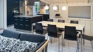 A modern kitchen with a central island, dining area with chairs, and a sofa with a floral-patterned cover. - Amazing home in Rørvig with sauna (Rørvig)