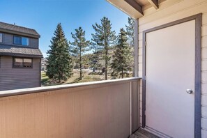 A balcony with a view of tall pine trees and a building in the background. - Sunridge 1061 W Beaver (Avon)