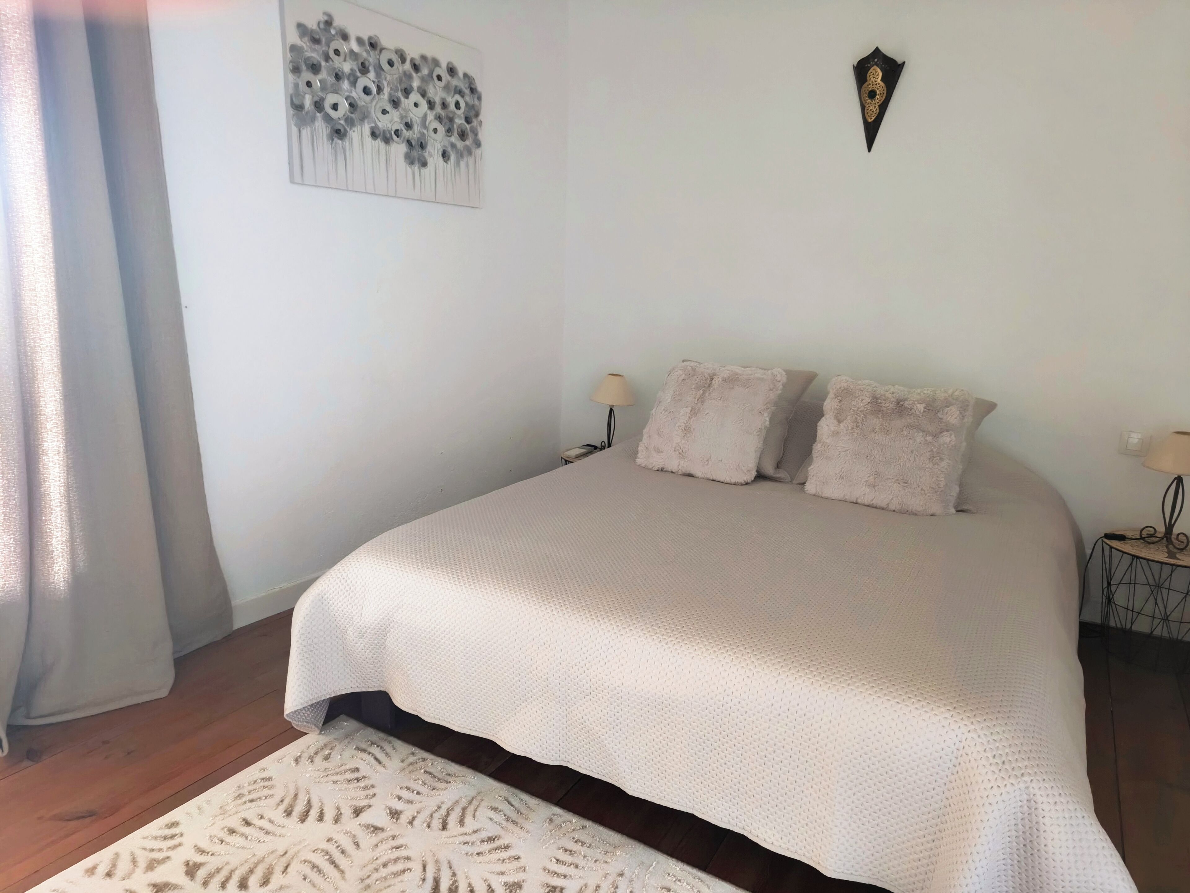 A bedroom with a bed, two pillows, a wall art piece, a decorative wall plate, and a nightstand with a lamp.