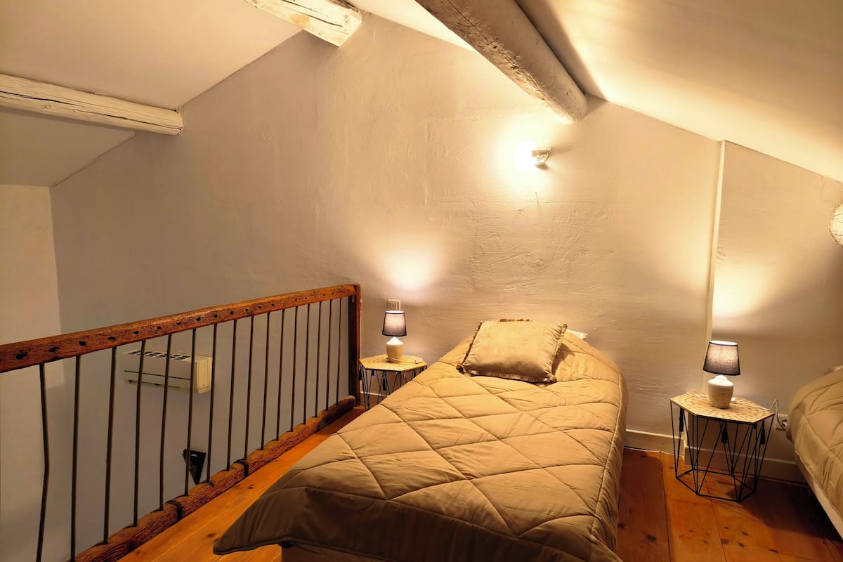 A bedroom with a wooden bed, two bedside lamps, a small table, and a sloped ceiling.