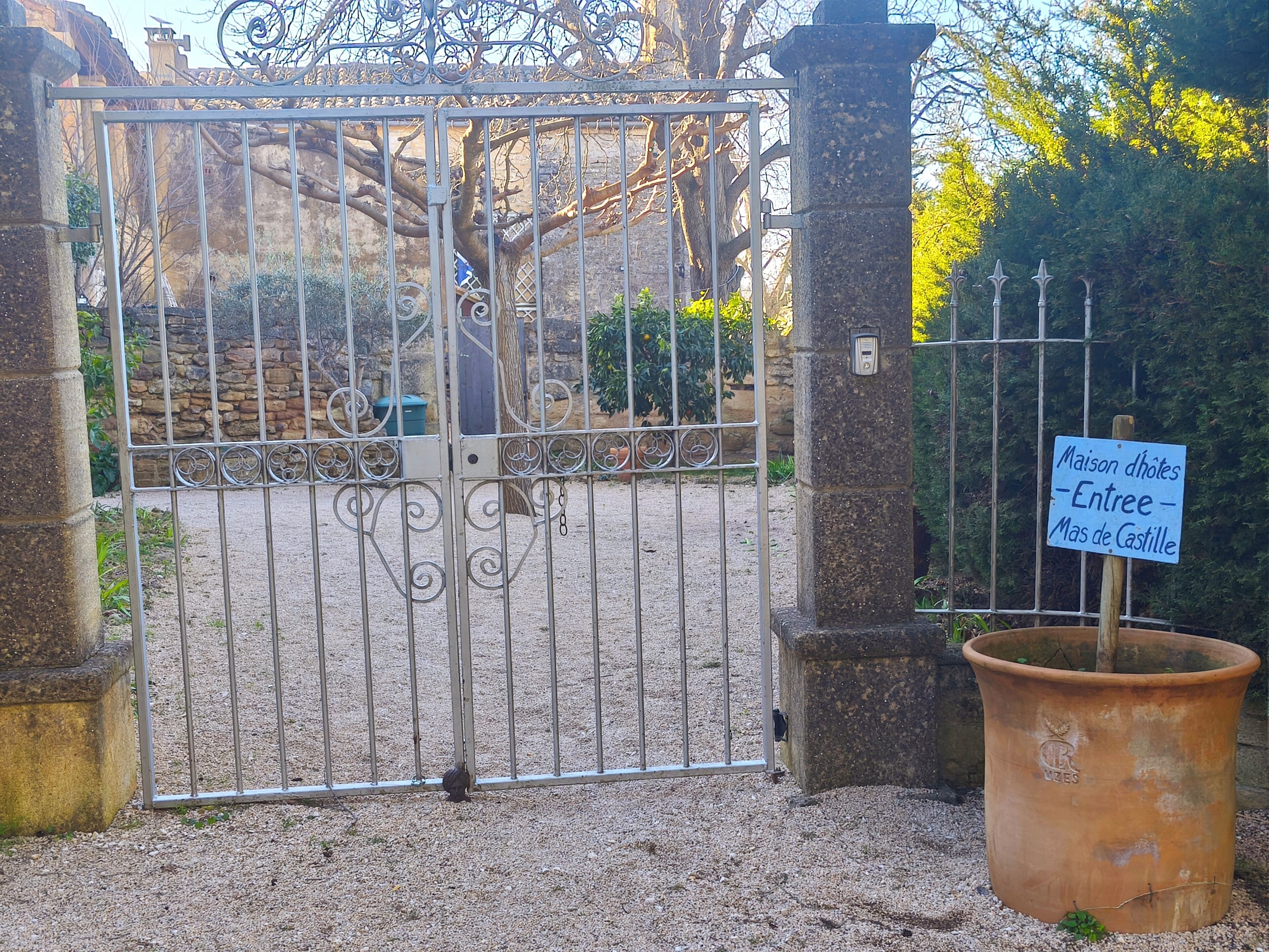 Ein verschlossenes Tor mit einem Metallgitter, einer Steinpfeiler und einem Schild, das den Eingang zum Maison d'Hoët – Entree – Mas de Castille kennzeichnet.