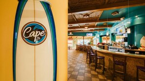 Interior de restaurante com placa de prancha de surf, área de bar e chão de azulejos.