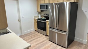 A compact kitchen with wooden cabinets, a stainless steel refrigerator, an oven, and a microwave. - Cozy 3/2 in downtown quaint Lake Mary, FL with AC and fenced in yard (Lake Mary)