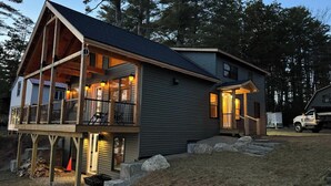 A two-story cabin with a balcony, a covered porch, and a truck parked outside. - Four seasons, waterfront, private beach! Elegant cozy cabin lakeside retreat! (Smithfield)
