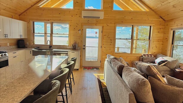 A spacious cabin interior with a high ceiling, a large kitchen area, and a cozy living room. - Four seasons, waterfront, private beach! Elegant cozy cabin lakeside retreat! (Smithfield)