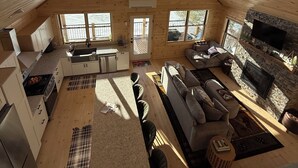 A spacious loft-style room with a kitchen, dining area, and living space. It features large windows, a stone fireplace, and a high ceiling. - Four seasons, waterfront, private beach! Elegant cozy cabin lakeside retreat! (Smithfield)