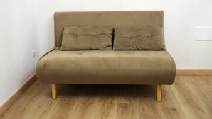 Un canapé beige aux pieds en bois, dans une pièce dont le sol est recouvert de parquet et les murs sont peints en blanc.