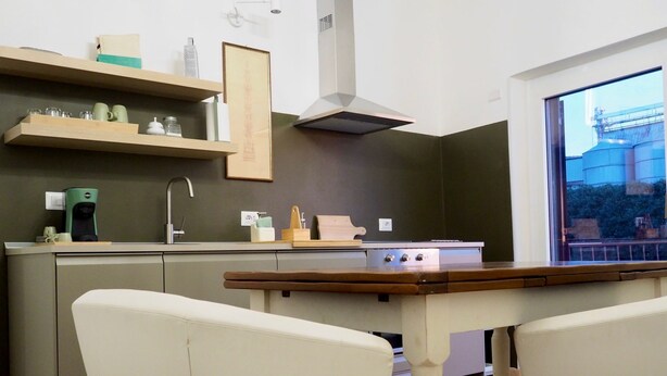 Une cuisine moderne dotée d’un îlot central, de meubles en bois et d’une grande fenêtre donnant sur des bâtiments industriels.