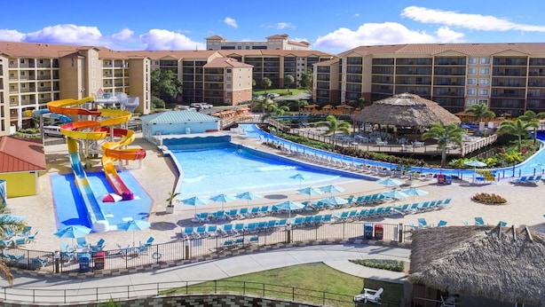 Un complex turístic amb una piscina gran, tobogans aquàtics i una construcció amb teulada de palla.
