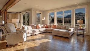 A spacious living room with a large sectional sofa, a wooden floor, and large windows offering a mountain view. - Fairway Twelve Retreat (Sun Valley)
