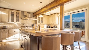 A spacious kitchen with a large island, wooden bar stools, and a view of the outdoors through large windows. - Fairway Twelve Retreat (Sun Valley)