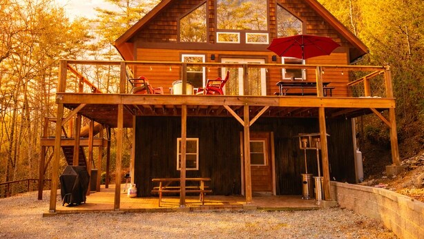 Una baita in legno con un balcone, una zona salotto esterna coperta e vista sulla foresta circostante.
