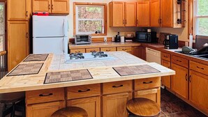 Una cucina spaziosa con mobili in legno, un'isola centrale con sgabelli, una lampada a sospensione e vista sull'esterno attraverso una finestra.
