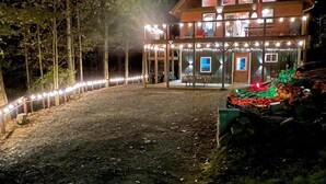 Una baita di legno a due piani con un balcone, circondata da un patio ben illuminato e luci decorative.