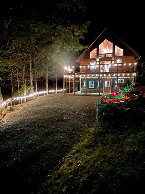 Eine zweistöckige Holzjagdhaus mit Balkon, umgeben von einer gut beleuchteten Terrasse und Lichterketten.