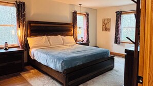 Una camera da letto con un letto grande, una testiera in legno, due comodini, un tavolino e una lampada a sospensione, oltre a una finestra con tende.