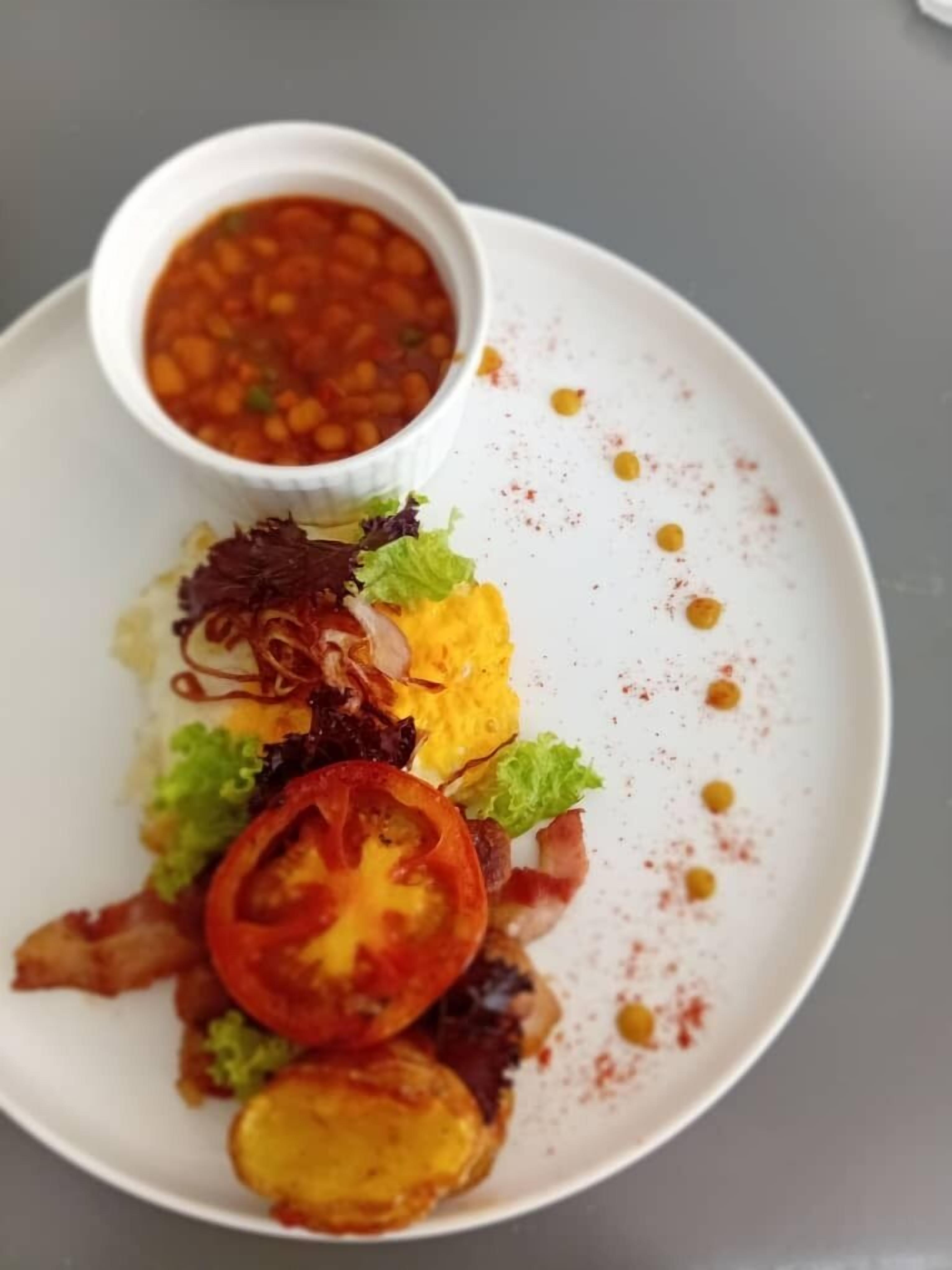 Un plato con ensalada, una rodaja de tomate y un recipiente pequeño de salsa.