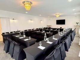 Un salón de conferencias con mesas largas, sillas y una araña.