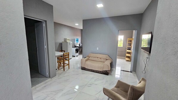 A spacious living area with a sofa, a dining table with chairs, a kitchen area with appliances, and a view through an open doorway. - Waterview Apartment w/Ocean Breezes Near Jeri (Preá - CE)