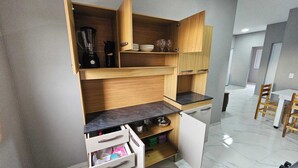 A compact kitchen with wooden cabinetry, a built-in dishwasher, and a dining area with a table and chairs. - Waterview Apartment w/Ocean Breezes Near Jeri (Preá - CE)