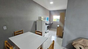 A compact kitchen with a refrigerator, microwave, and sink. There is a dining table with chairs, and a wooden cabinet. - Waterview Apartment w/Ocean Breezes Near Jeri (Preá - CE)