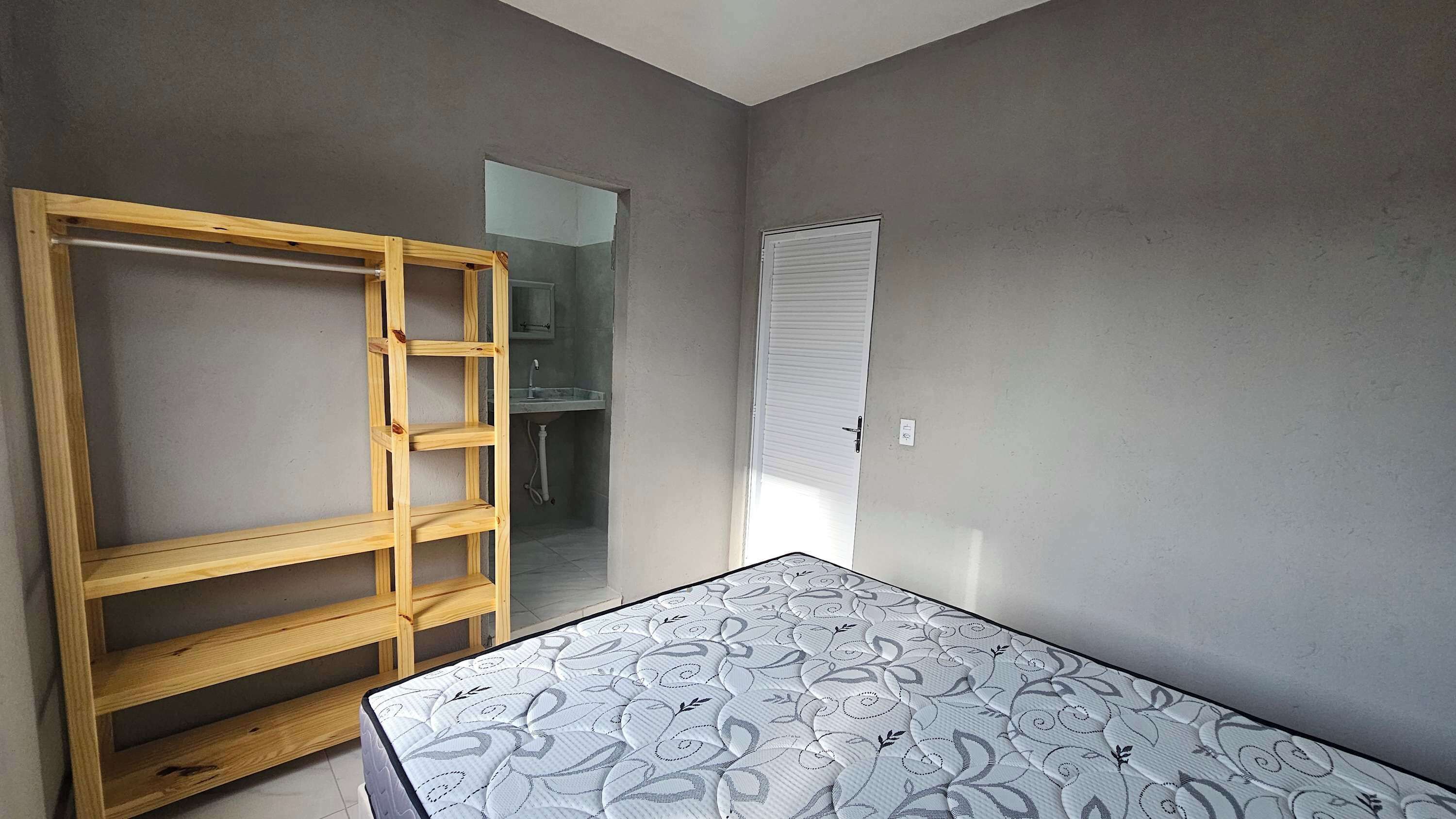 Une chambre avec une échelle en bois, un matelas à motifs, une fenêtre avec des stores et une porte donnant sur une autre pièce.