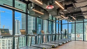 A gym with treadmills aligned against a wall with large windows overlooking a cityscape. - Luxury Miami Studio with Rooftop Pool (Miami)