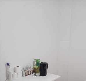 A white table with a spray bottle, toilet paper, a box of tissues, a glass, and a black kettle. - Cosy double bedroom near Eurostar & KX (London)