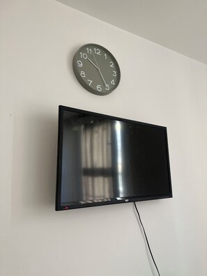 A wall-mounted flat-screen TV and a round analog clock above it. - Cosy double bedroom near Eurostar & KX (London)