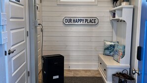 A hallway with a sign reading "OUR HAPPY PLACE," a small window, a bench with cushions, and a trash bin. - Topsail Beach Sunsets, Water views, Pool/Hot tub (N. Topsail Beach)