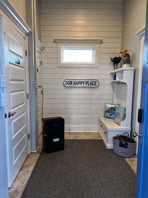 A hallway with a sign reading "OUR HAPPY PLACE," a small window, a bench with cushions, and a trash bin. - Topsail Beach Sunsets, Water views, Pool/Hot tub (N. Topsail Beach)