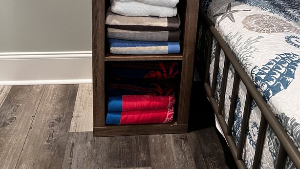 A wooden shelf with folded towels in various colors, a seahorse lamp, and a bed with a patterned bedspread. - Topsail Beach Sunsets, Water views, Pool/Hot tub (N. Topsail Beach)