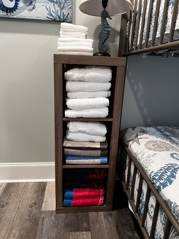 A wooden shelf with folded towels in various colors, a seahorse lamp, and a bed with a patterned bedspread. - Topsail Beach Sunsets, Water views, Pool/Hot tub (N. Topsail Beach)