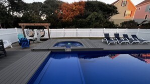 Ein Schwimmbecken mit Holzterrasse, Liegestühlen und einem Whirlpool.