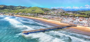 Une ville côtière dotée d’une jetée qui s’avance dans la mer, entourée de collines et de bâtiments.