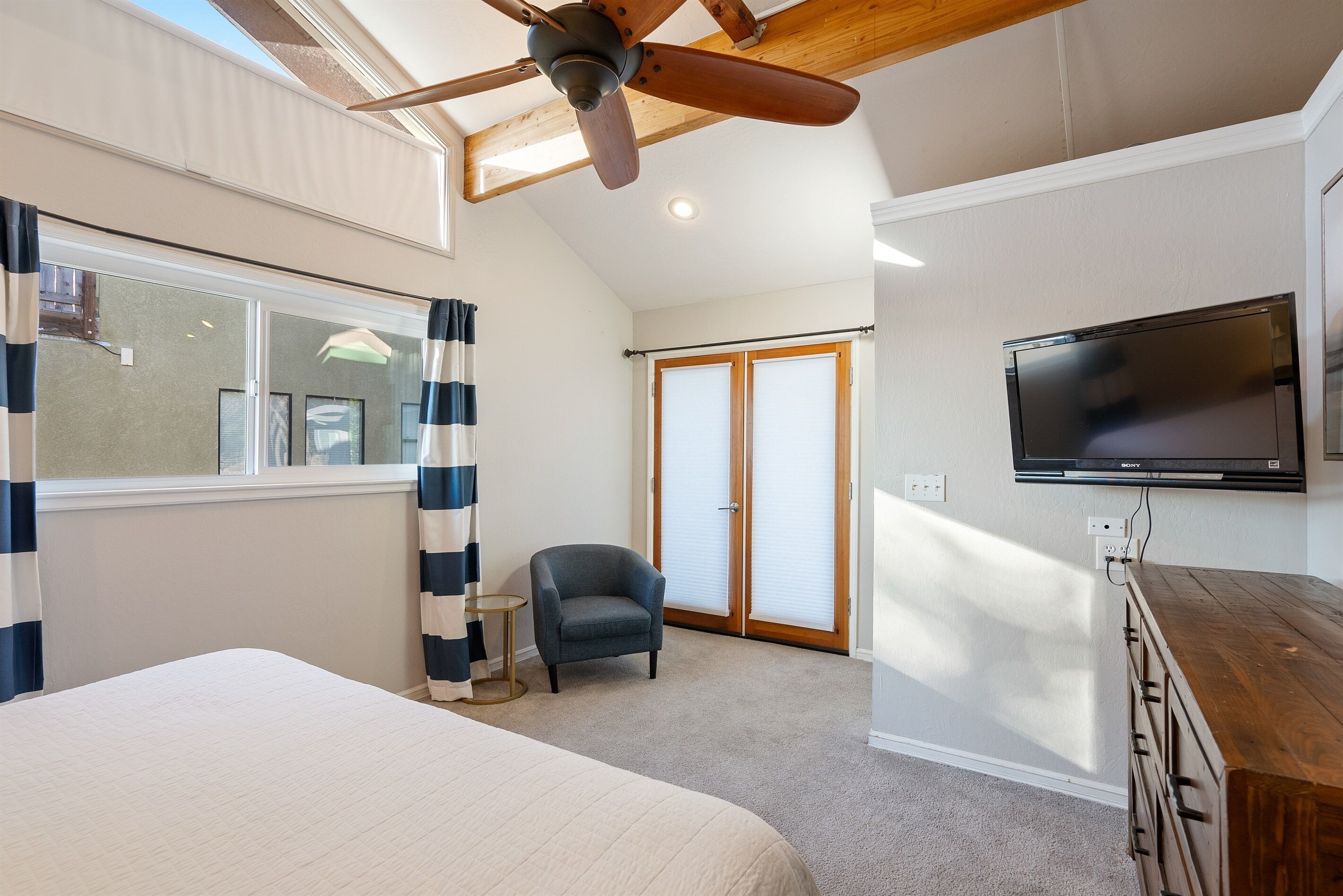 Une chambre à coucher avec un lit, une chaise, un téléviseur et un ventilateur de plafond.