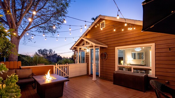 Eine Holzterrasse mit Feuerschale, Sitzgelegenheiten im Freien und Lichterketten.