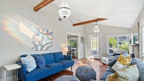 Ein geräumiges Wohnzimmer mit einem blauen Sofa, Poufs und einer Kristallleuchter.
