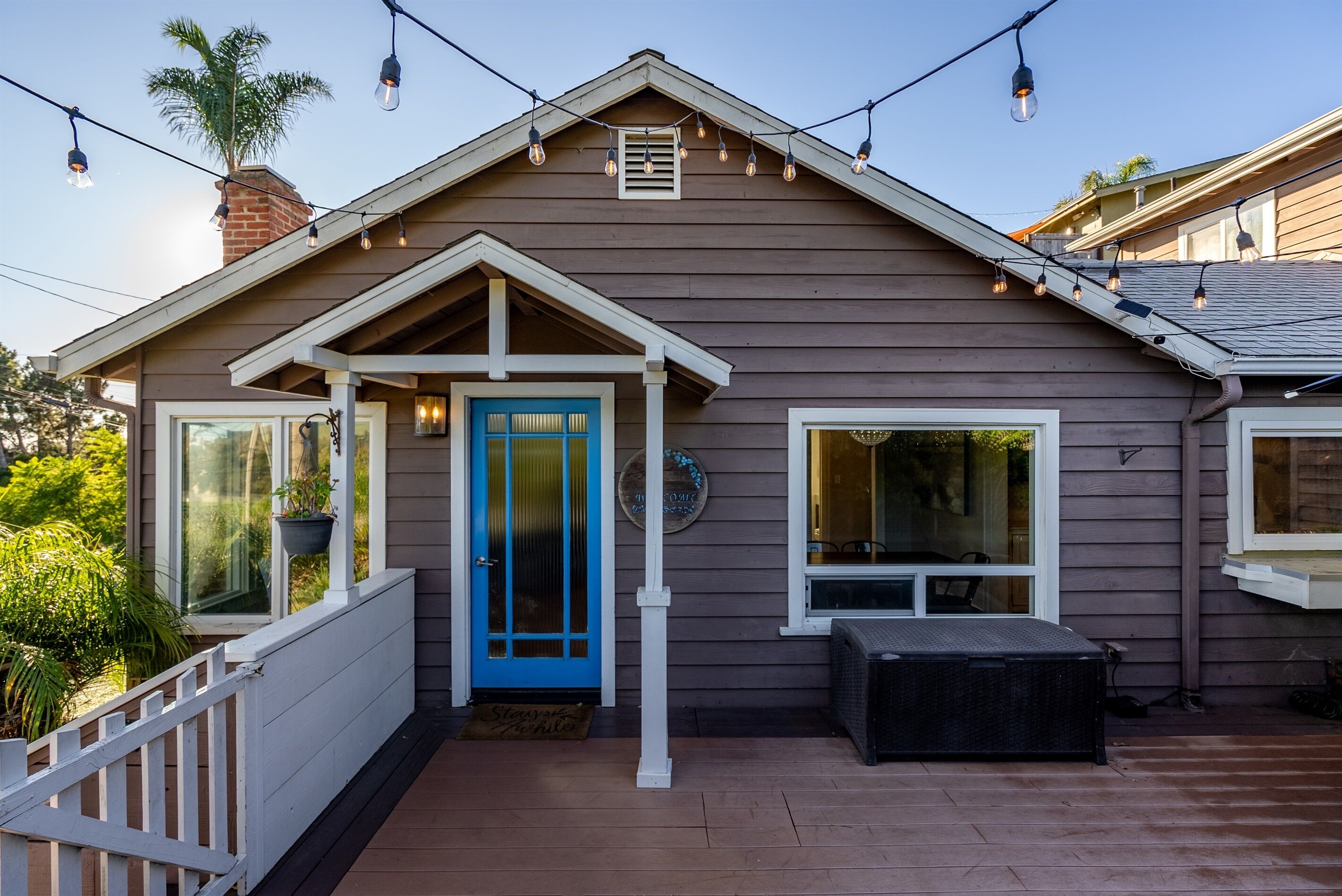 A house with a blue door, a porch with a bench, and string lights.
