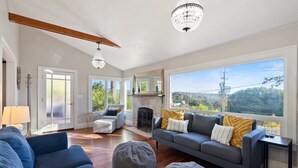 Ein geräumiges Wohnzimmer mit grauem Sofa, blauen Sessel und einem großen Fenster mit Blick auf Grünflächen.