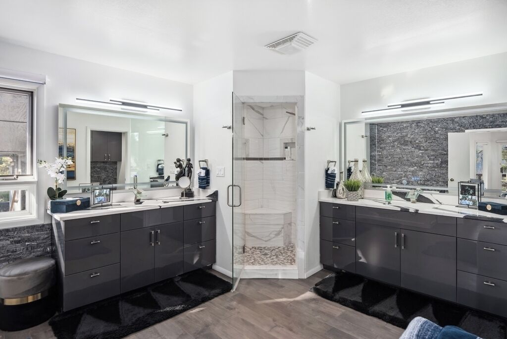 Een moderne badkamer met dubbele wastafels, een douchecabine van glas en een marmeren spatwand.
