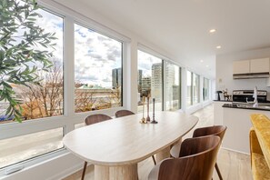 A modern kitchen with a large window, a dining table with chairs, and a view of the cityscape. - Montréal Downtown Haven | Walk to All Attractions (Montréal)