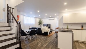 A modern apartment with a staircase, a dining area, a living room with a sofa, a kitchen with a bar, and a large window. - Chic City Hideaway | Vibrant Heart of Montréal (Montreal)