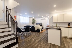 A modern apartment with a staircase, a dining area, a living room with a sofa, a kitchen with a bar, and a large window. - Chic City Hideaway | Vibrant Heart of Montréal (Montreal)