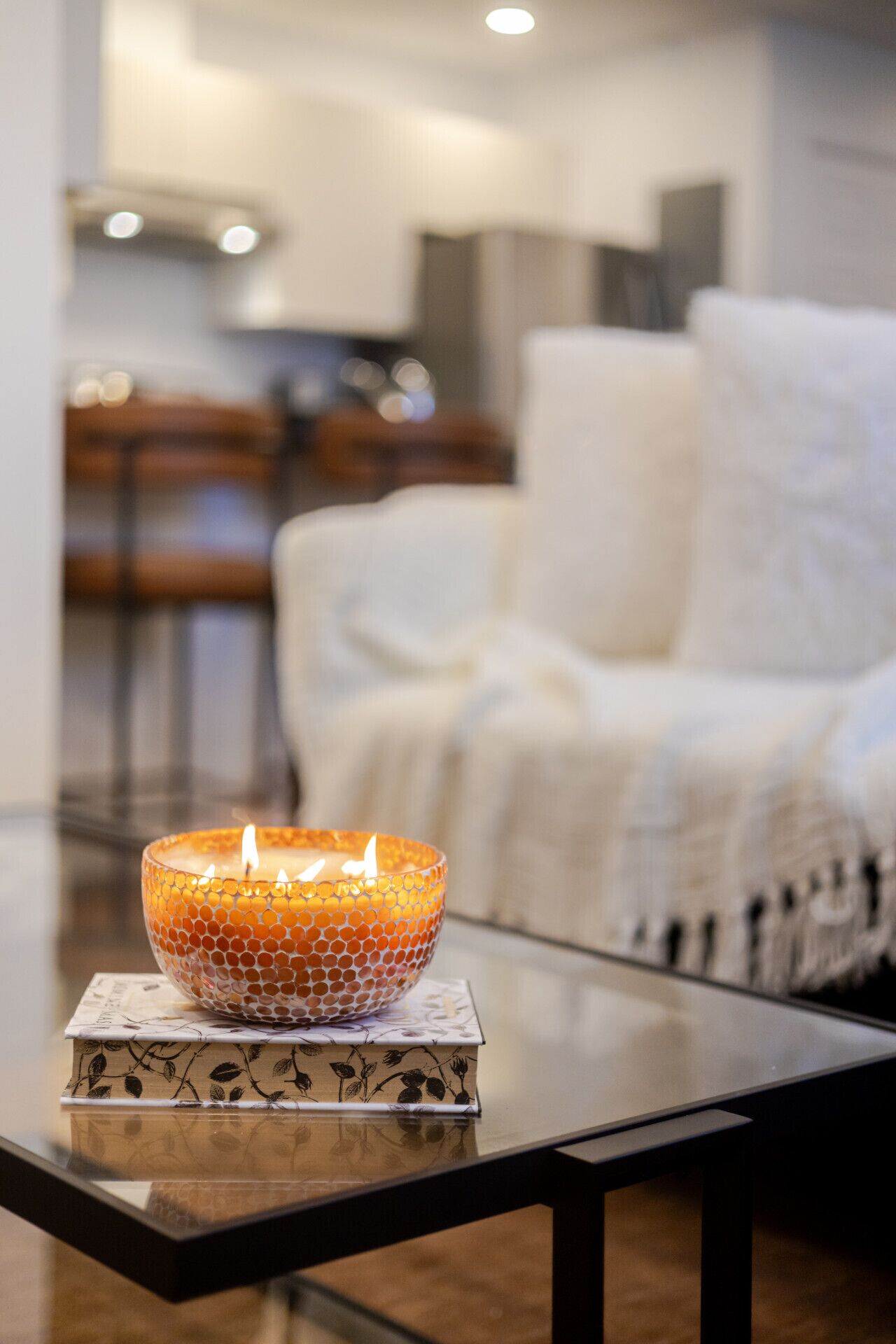 Una vela sobre una mesa en un salón moderno con un sofá y una cocina al fondo.