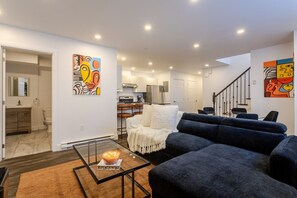 A modern living room with a sofa, a glass coffee table, and abstract art on the walls. - Chic City Hideaway | Vibrant Heart of Montréal (Montreal)