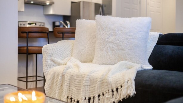 A living room with a sofa, a chair, and a table with a candle. - Chic City Hideaway | Vibrant Heart of Montréal (Montreal)