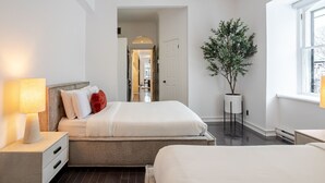 A hotel room with a bed, a nightstand, a lamp, a potted plant, and a window. - Elegant Downtown Stay | Near Bell Centre MTL (Montreal)