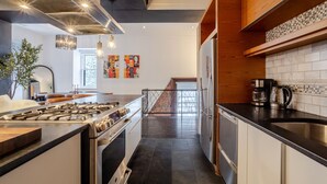 A modern kitchen with a gas stove, stainless steel appliances, and a wooden accent wall. - Elegant Downtown Stay | Near Bell Centre MTL (Montreal)